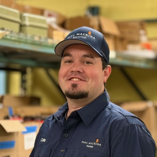 Paul Macrina Electrical team member in navy cap and work uniform in warehouse facility background